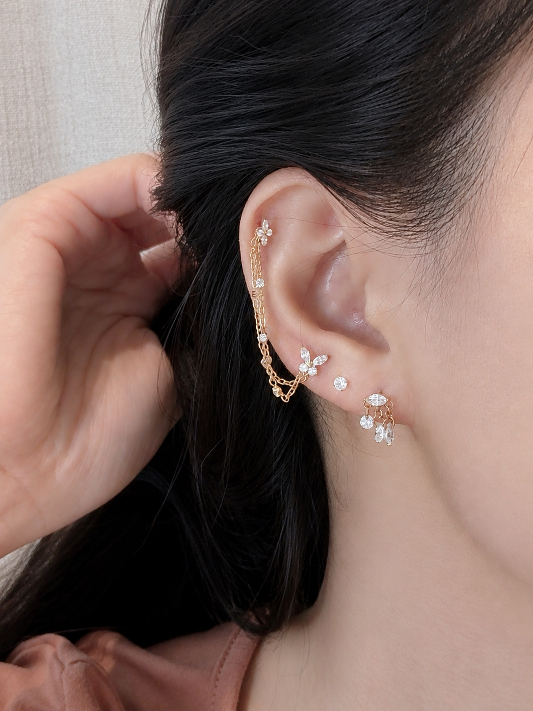 A close-up of a person's ear wearing a gold ear cuff with small clear stones and matching stud earrings.