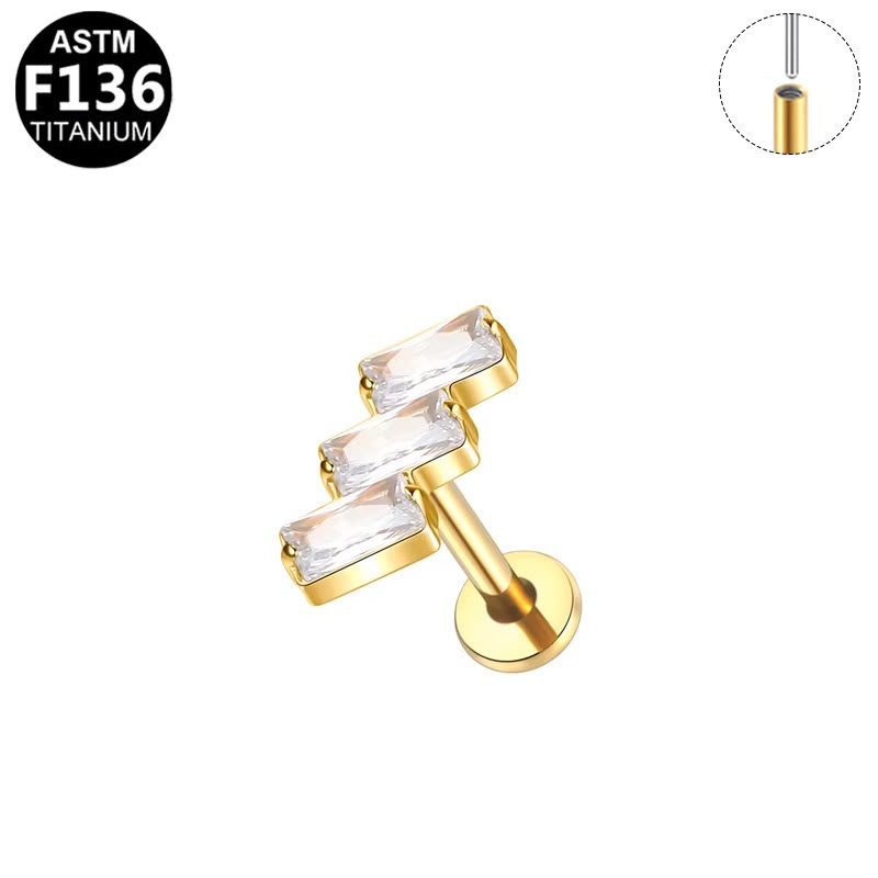 Gold-plated titanium ear cuff with three clear rectangular bezel-set crystals, shown on a white background with an inset diagram and an ASTM F136 titanium badge.