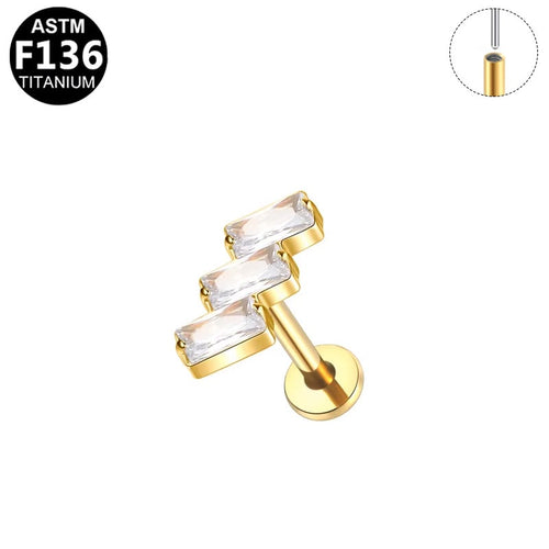 Gold-plated titanium ear cuff with three clear rectangular bezel-set crystals, shown on a white background with an inset diagram and an ASTM F136 titanium badge.