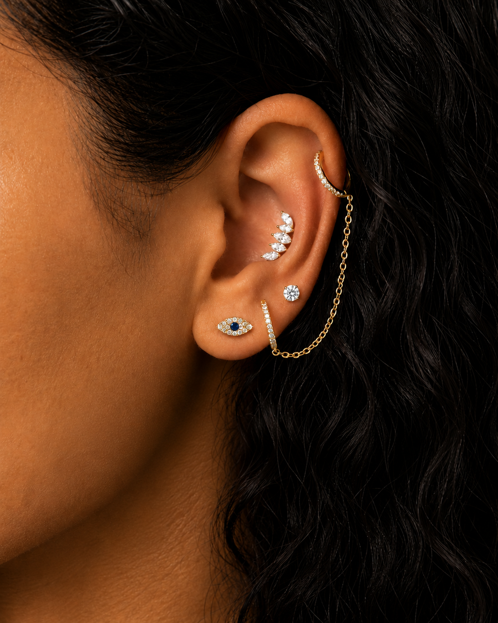 Woman wearing Marquise cluster stud earring close-up, evil eye earring and 1 pair of double huggies that hug the ear lobe and helix.