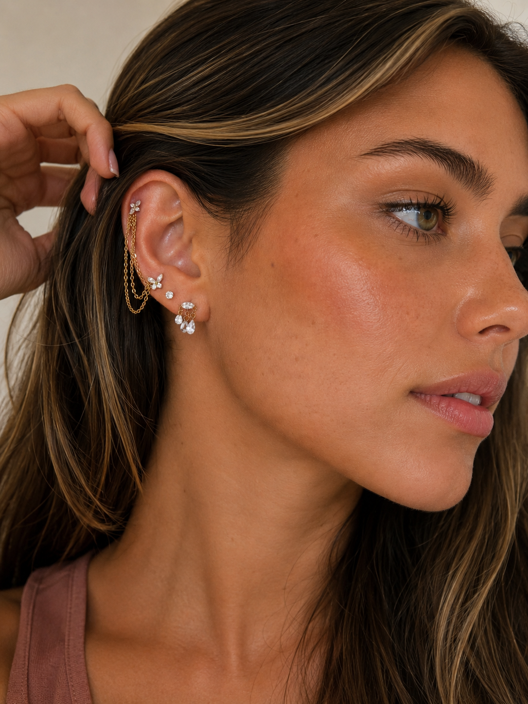 A close-up of a model's ear showcasing a multi-piece gold ear cuff set adorned with clear crystals. The set includes a flat ear cuff with hanging chains, butterfly studs, a small stud, and a cluster drop earring.
