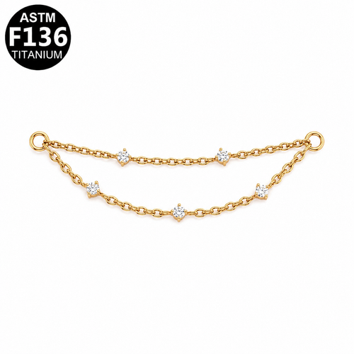 A gold-toned double-chain bracelet with small solitaire, star-shaped clear gemstone accents, shown on a white background with an ASTM F136 Titanium badge in the top-left corner.