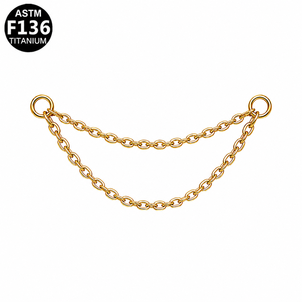 A gold-toned double-strand chain link accessory with two circular ring ends, shown on a plain white background with an ASTM F136 Titanium badge in the top-left corner.