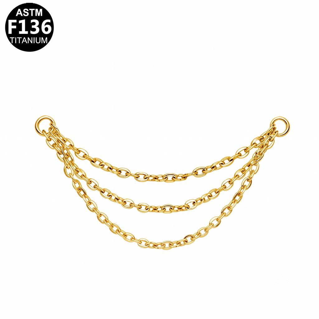 A gold-toned three-strand chain accessory with oval links and circular end rings, shown on a plain white background. A black circular badge in the top-left corner reads 'ASTM F136 TITANIUM'.